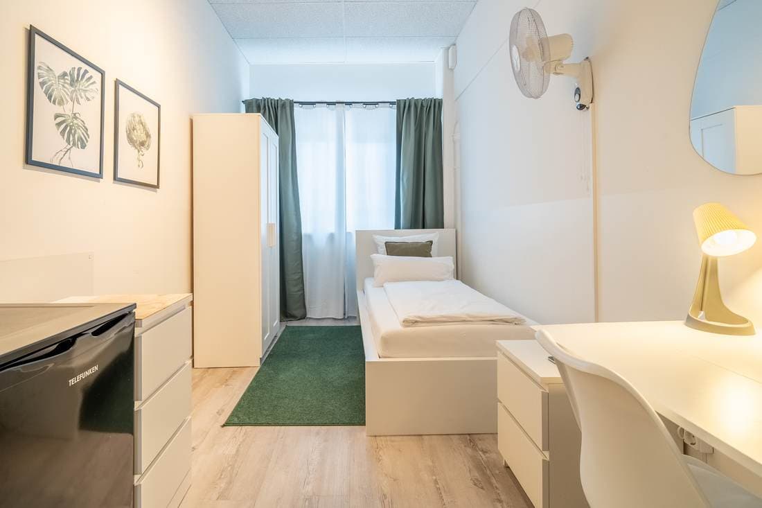 Einzelzimmer mit Schreibtisch und Ventilator